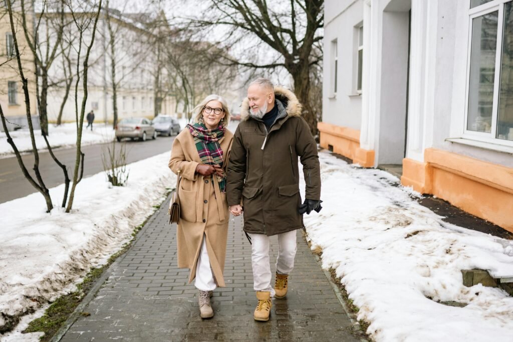 Elderly couple walking hand in hand on an urban snowy sidewalk, showcasing love and connection.